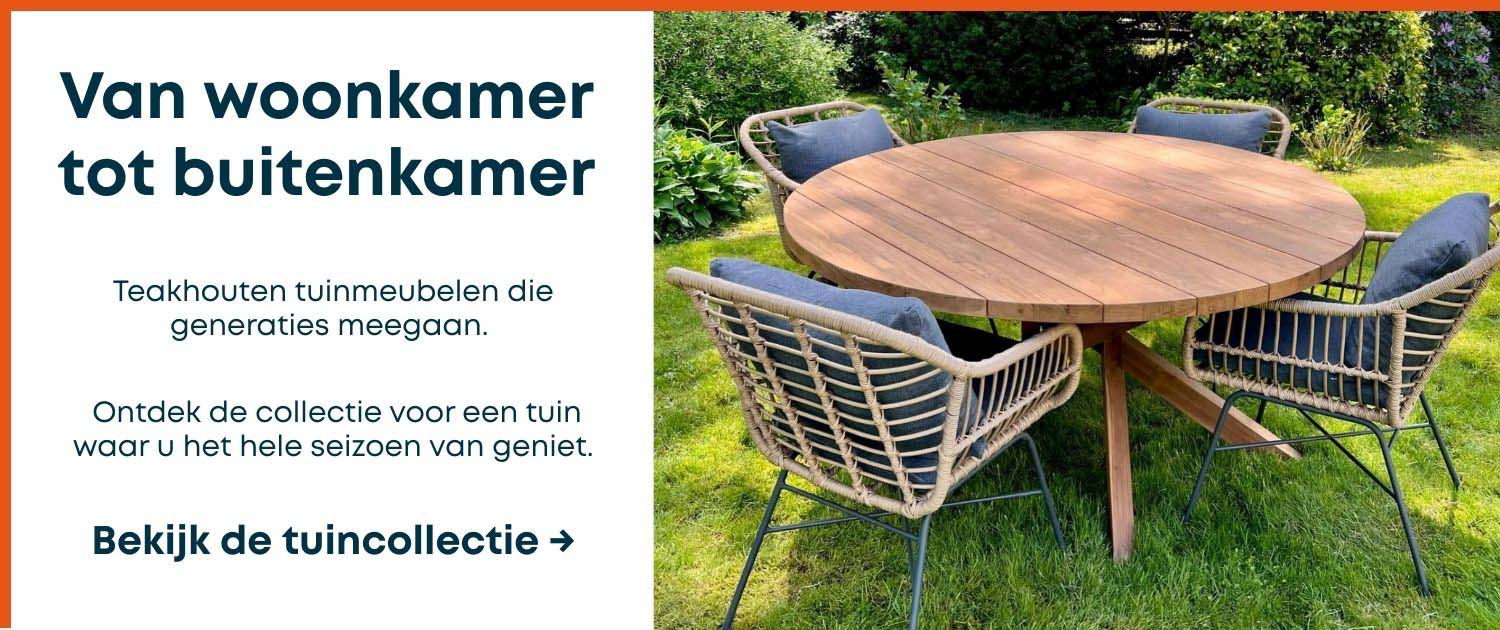teakhouten-tuinmeubelen-collectie Ronde teakhouten tuintafel met vier gevlochten stoelen met donkergrijze kussens, opgesteld op een groen gazon omringd door weelderige tuinbeplanting